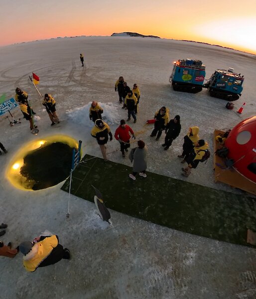 An aerial shot of a round pool in the ice with fake grass and some small huts