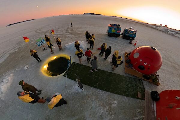 An aerial shot of a round pool in the ice with fake grass and some small huts