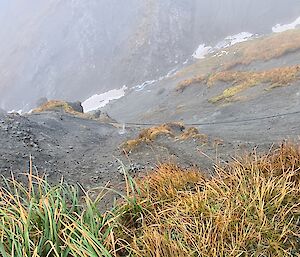 Water rushes from a hole in a black water pipe that travels above ground across the rocks