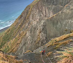 Two people are roped up to repair a water pipe half way down a hill