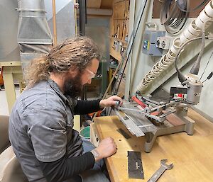 Man sitting at bench, wearing safety glasses is working a machine