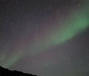 An aurora in purple and green with a hill and aerial in the foreground