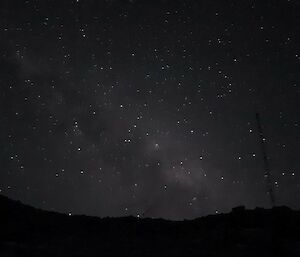 A distant hill with dark sky and plenty of stars