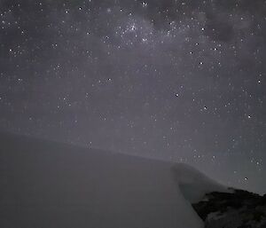 A sky full of stars with snow and rocks in the foreground