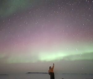A purple and green sky with a person holding one arm up in the foreground