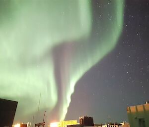 An aurora's green ribbons sitting above some station buildings