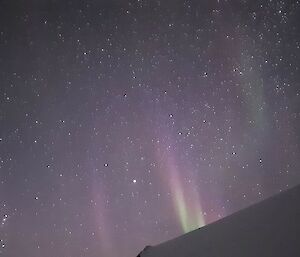 A purple and green faint aurora with many stars in the background