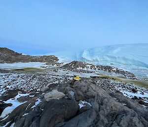 Person sitting with their back to the camera, looking out across valley with emperor penguin rookery and glacier in distance