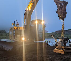 A yellow excavator lifts a smaller machine into place on a foggy day