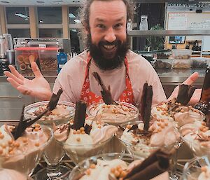 Man wearing large smile stands behind a selection of glasses filled with chocolate mousse