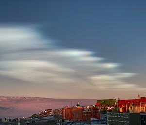 Whispy pearlescent clouds cover 2/3 of sky over looking station buildings