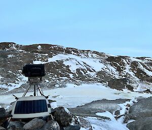 Camera on tripod on rocky outcrop overlooking small rocky valley empty of penguins