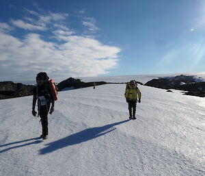 A couple of people walking with back packs on packed down snow on a hill