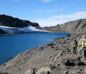 A group of people walking on rocks next to a large blue lake