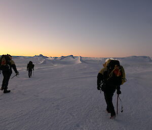 A group of people walking on the sea ice near icebergs
