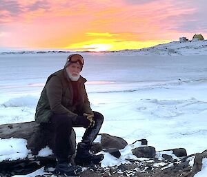 a man sitting on a rock with the sunrising in the background