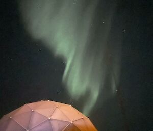 A green aurora in a dark sky over a round building