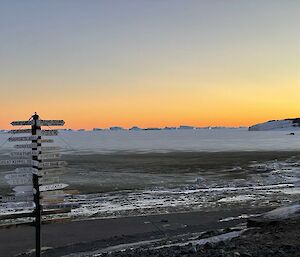 Street sign posted to many locations looking out on dirty ice with icebergs in the background