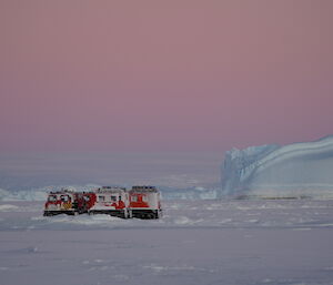 Two hagglunds vehicles parked on sea-ice with iceberg on background and beautiful pink light of twilight above