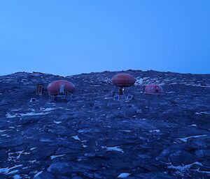 Two round red huts positioned on rocky ground