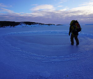 man wearing pack walks across sea-ice