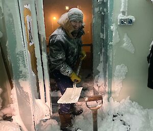 Cold porch filled with snow, man stands at open door with shovel