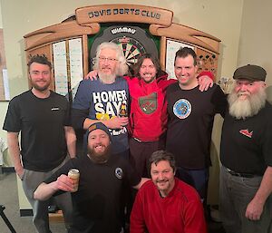 A group of men smiling in front of a dart board