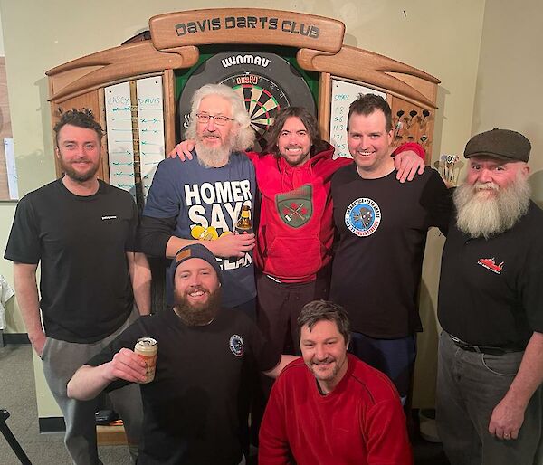 A group of men smiling in front of a dart board