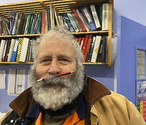 An electrician with tools in his pockets, standing in an office room, has threaded a pencil into his thick moustache