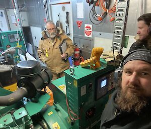 Three men wearing ear muffs working in an industrial engine room