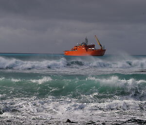 A large red ship sits out to sea with rough waves coming onshore