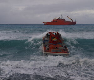 A small barge heads out to sea towards a large red ship