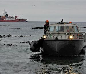 A silver barge comes ashore as a red and white ship sits offshore