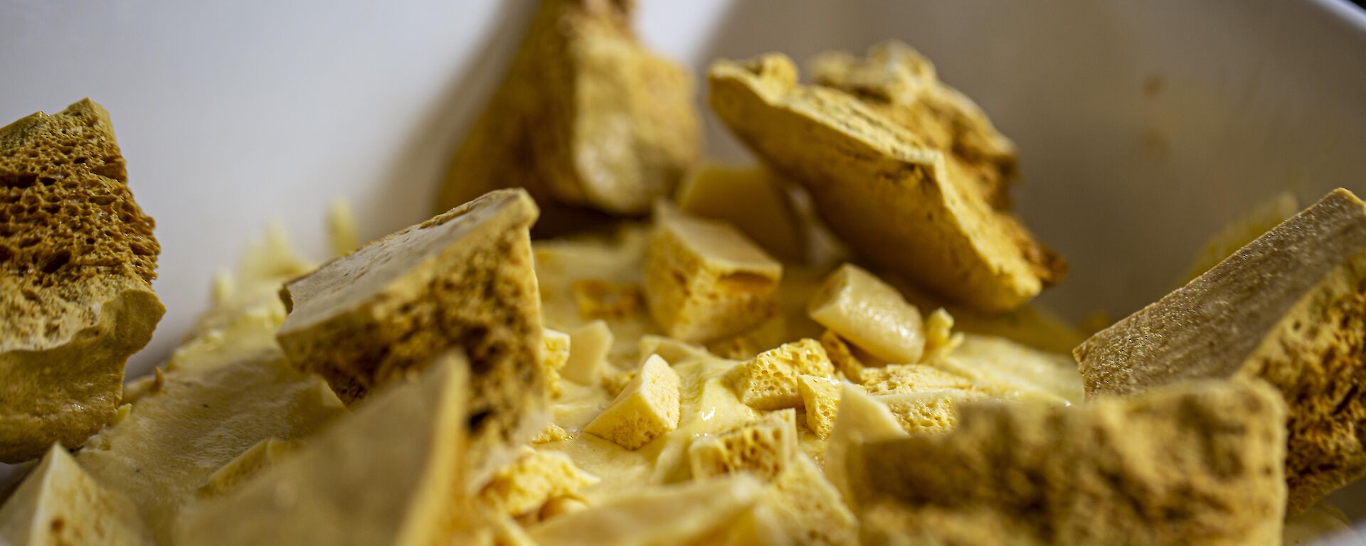 A close-up view of broken pieces of honeycomb confectionery. The light yellow chunks vary in size, have jagged edges and a porous texture