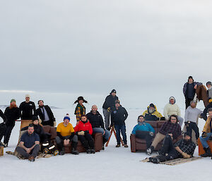 A group of people sitting and standing on furniture the ice in various clothes not smiling
