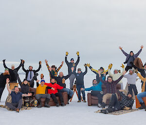 A group of people standing and sitting on furniture on the sea ice with their hands in the air