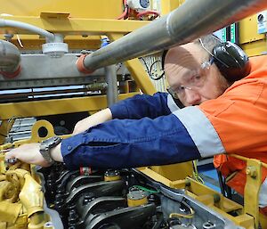 Man in high vis and wearing protective glasses and ear protection leans over a large engine and conducts adjustment.