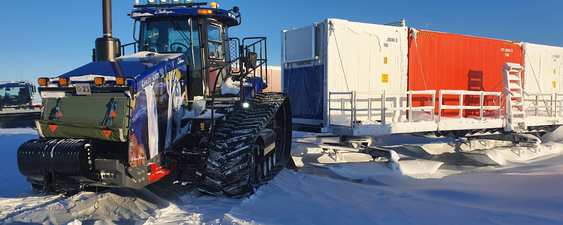 A tractor hitched to a row of large cargo containers mounted on sleds, ready to pull them across the snow