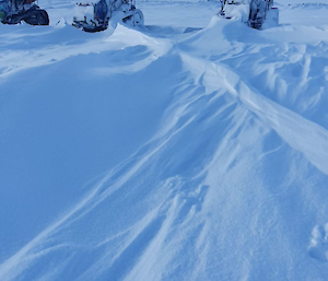 Three tractors parked in a snowy field. Snow on the ground is formed in long, low ridges, indicating there has recently been very strong wind. Two of the tractors have substantial snow build-up on their bonnets, windshields, tracks and wheels.