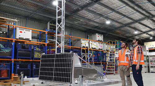 Two men examine the ARTEMIS system. Which shows a solar panel connect to metal framework.