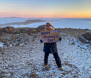 Alana standing on a hill with sea ice behind holding a Happy Mother's Day sign