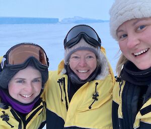 Three women smiling for the camera with Auster emperor penguin colony behind