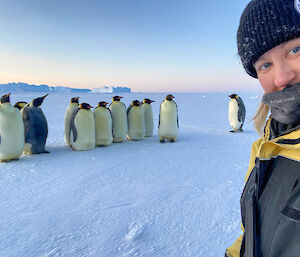 Alana sitting on the ground with a group of emperor penguins behind