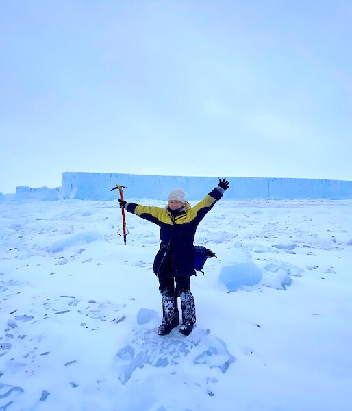 Alana standing in front of an iceberg with arms in the air