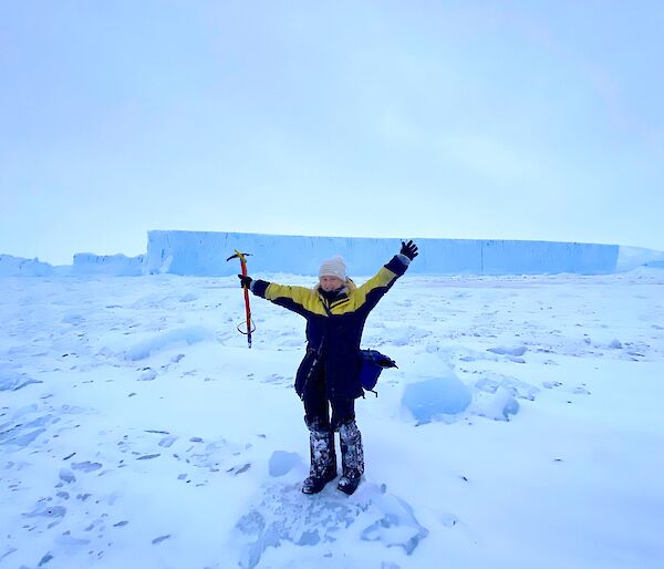 Alana standing in front of an iceberg with arms in the air