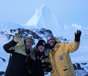 Three people in cold weather gear, standing in front of a big ice berg at Macey