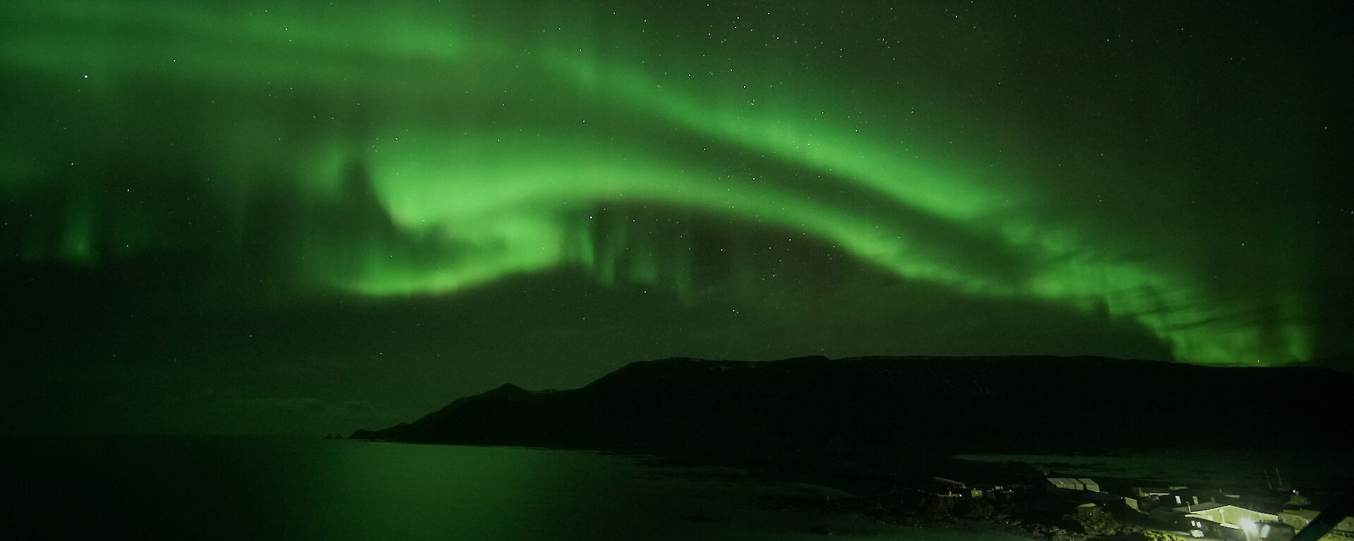 A green aurora lightsup the sky over part of the island and the ocean