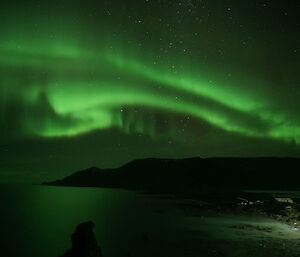 A green aurora lightsup the sky over part of the island and the ocean
