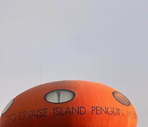 Close up of hut, which is red and round on stilts, so called a googie. Has written on it "Béchervaise island penguin monitoring"