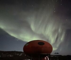 Googie hut in centre front with green aurora above and bright stars in the sky